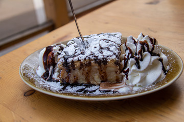Apple pie sprinkled with powdered sugar, served with ice cream and whipped cream, topped with chocolate sauce