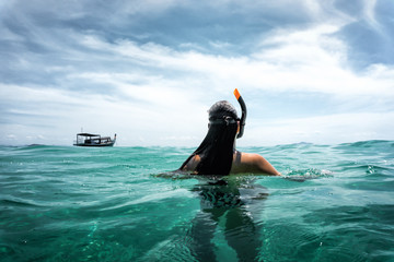 young woman from behind swims in the open sea while snorkeling with blue sky and clouds during summer trip