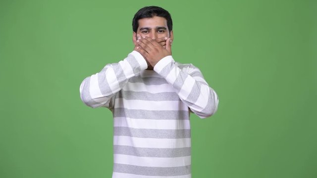 Young handsome Persian man covering mouth as three wise monkeys concept