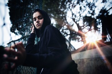 Anxious teenage girl leaning on wire mesh fence at school campus