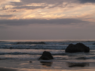 Fototapeta na wymiar Puesta de sol entre nubes en playa rocosa.