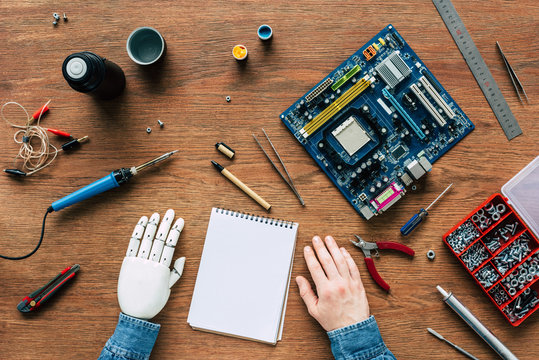cropped image of man with prosthetic arm at table with textbook, instruments and motherboard