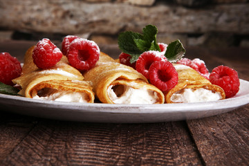 Homemade crepes served with fresh raspberrries and powdered sugar on rustic wooden table