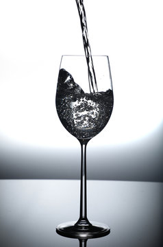 clear water being poured in tall wine glass with splash and bubbles