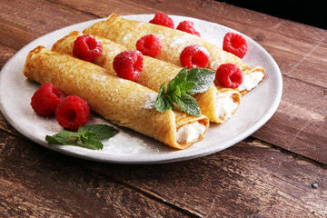 Homemade crepes served with fresh raspberrries and powdered sugar on rustic wooden table