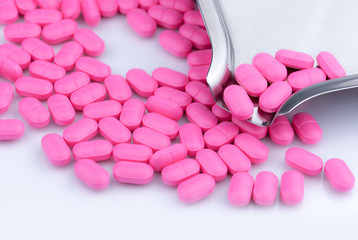 Pile of pink tablets pill on white background near stainless steel drug tray. Norfloxacin 400 mg...