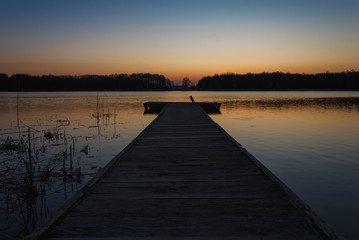 Naklejka premium Ciemna sylwetka molo na tle jeziora, w którym odbija się wieczorne niebo. Po zachodzie słońca