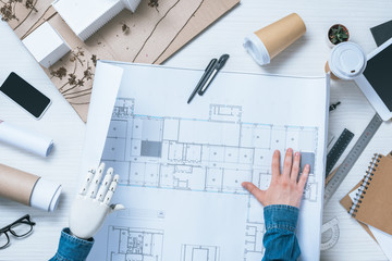 partial view of male architect with prosthetic arm looking at blueprint
