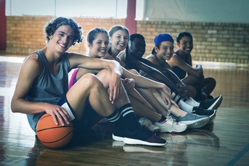 High school kids sitting on the floor in basketball court - Powered by Adobe