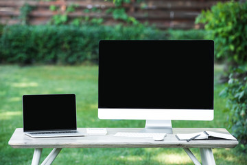 selective focus of textbook, laptop and computer with blank screens at table outdoors