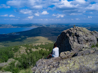 Brave girl sitting on the edge of the huge stone