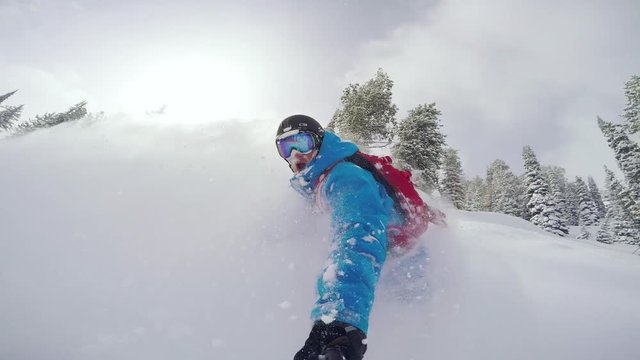A snowboarder carves into waist deep powder on a blue bird day