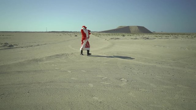 Russian Santa Claus or Ded Moroz with sack walks on sand, found asphalt road in desert, comes, coming to town for Christmas at summer in Africa, UAE
