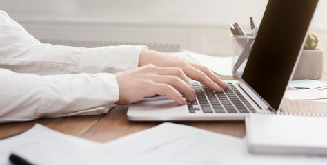 Side view of woman's hands typing on laptop keyboard
