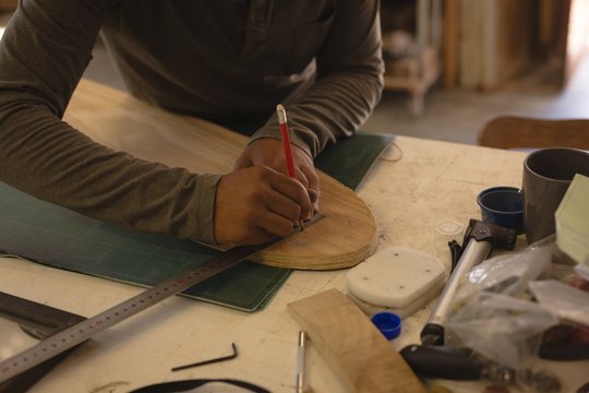 Midsection of man marking on skateboard in workshop