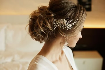 Foto auf Alu-Dibond Hochzeitsfrisur eines schönen und modischen braunhaarigen Modellmädchens in einem Spitzenkleid, mit Ohrringen und Schmuck im Haar © innarevyako