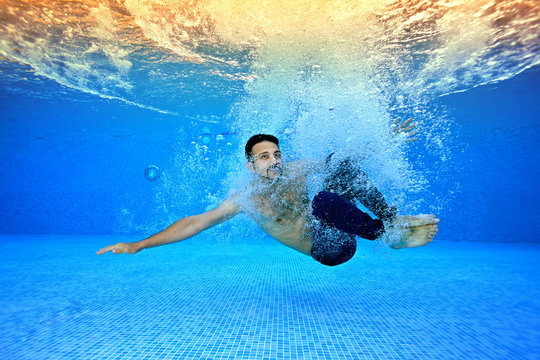 A young guy plunges into the water at the bottom of the pool on the background of sunlight in air bubbles. Portrait. Underwater photography. Landscape orientation