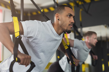 Men performing TRX training in gym