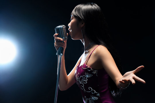 Asian woman singer holding a microphone singing.