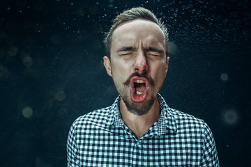 Young handsome man with beard sneezing, studio portrait