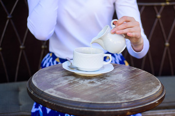 With milk tastes better. Tips for healthier coffee drinking. Hand female adding pouring milk to black coffee outdoors cafe terrace, close up. Mug americano or black coffee and jug with milk