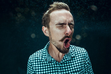 Young handsome man with beard sneezing, studio portrait
