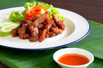 Fried dry piece pork with red chili sauce delicious thai food eaten with sticky rice in white dish on banana leaf