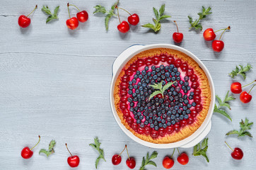 Delicious bluberry pie in the baking dish on the gray kitchen background with copy space for text. Homemade cheesecake decorated with ingredients - cherries and mint. Top view