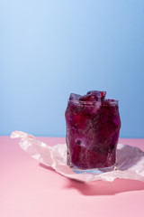 Frozen icy red berries in a glass on crumpled wrapping paper standing on a pink table on a blue background