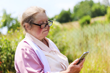 Elderly woman in the street wearing glasses looks at the mobile phone