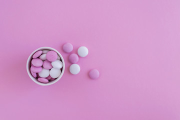 Pink and white round candies in cup on pink background