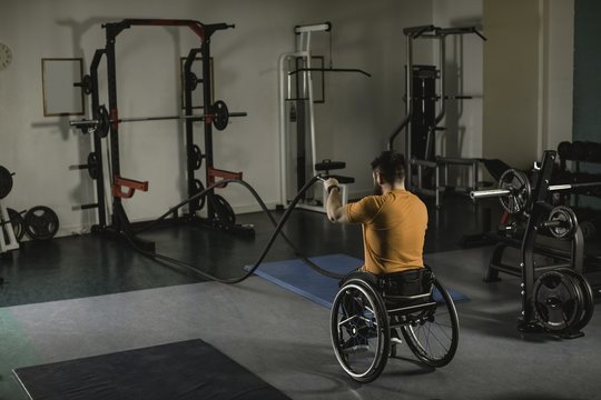 Handicapped man on wheelchair exercising with battle ropes in gym