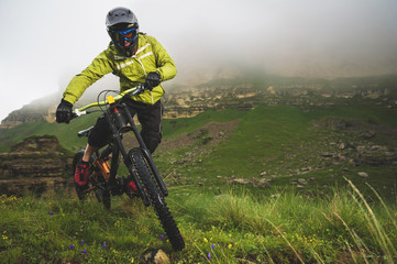 Fototapeta na wymiar A man in a mountain helmet riding a mountain bike rides around the beautiful nature in cloudy weather. downhill