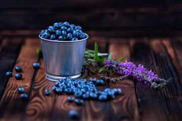 blueberries in a bucket on a dark wooden background .field flowers. rustic style