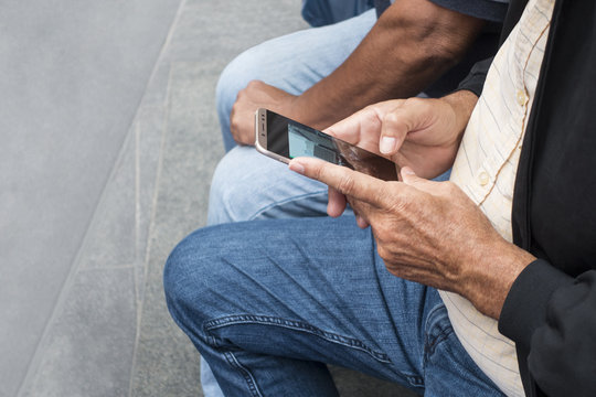 older man sitting on a bench holding and looking at his cell phone  with people sitting next to him