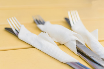 Cutlery wrapped in a paper napkin on a yellow wooden background.