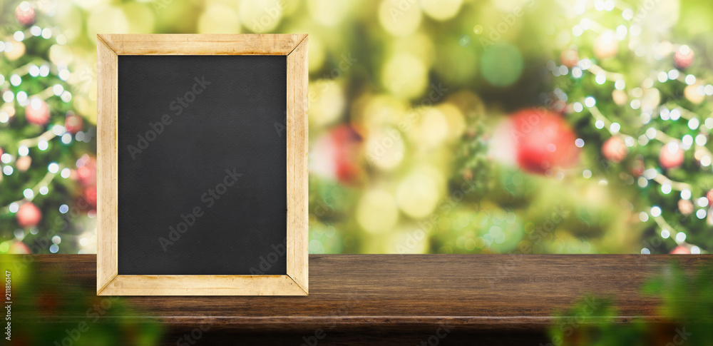 Poster blackboard on dark brown wood table top with abstract blur christmas tree red decor ball and snow fa