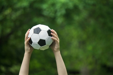 soccer ball in outstretched hands on a green background of nature