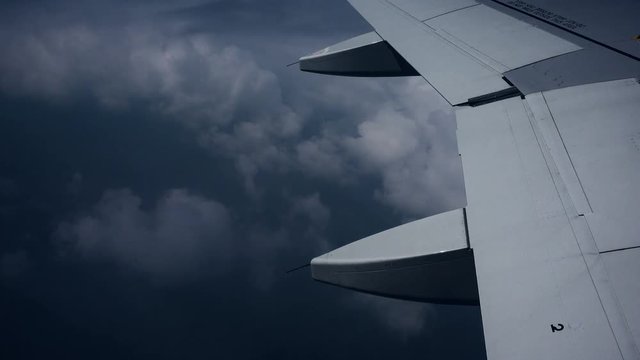 Wing of an airplane flying in the dark clouds. View sky from the window of airplane
