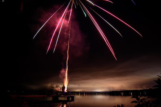 Fireworks over the water on dock with horizon over lake and people in silhouette