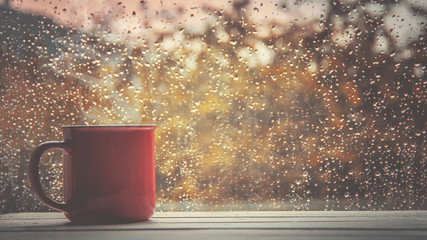A cup of hot tea in the background rain outside the window. Selective focus. 