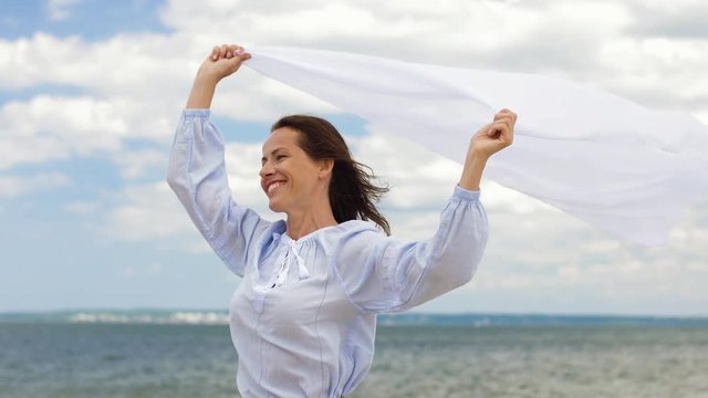 people and leisure concept - happy woman with shawl waving in wind on summer beach