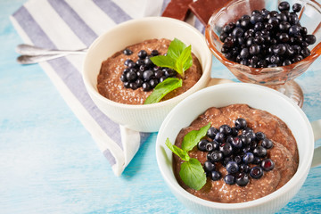 Healthy breakfast, two bowls with Chia seed pudding with berries and carob on blue wooden table. vitamin snack, diet and healthy eating