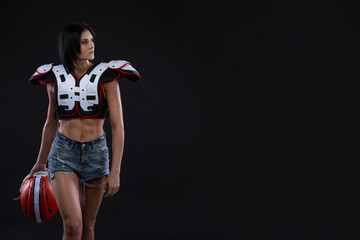 incredibly beautiful, athletic brunette girl in a shoulderpads and an American football helmet demonstrating stunning amazing abs. Black background. Footy. Sexy. Having fun. Rugby