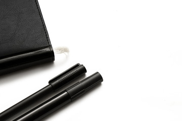 Black diary and 2 pens on a white background