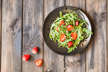 Fresh salad with arugula and strawbery with balsamic sauce and pine nuts. Vegetarian food. Salad with berries. Vitamin food, diet salad on wooden background in black plate.