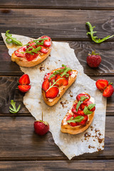 Italian bruschetta with cream cheese, strawberry, arugula and balsamic vinegar sauce with honey. Appetizer with chiabatta bread and strawberry on wooden background. Italian breakfast. Italian cuisine.