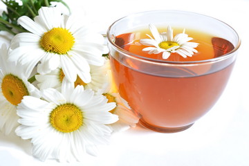 bouquet of field chamomile and glass transparent cup of brown warm tea