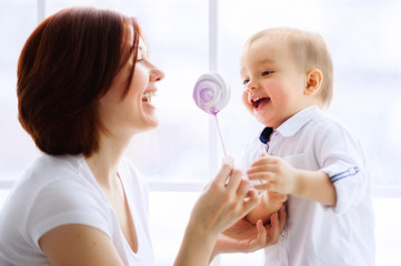 Mother giving her toddler son a meringue candy on stick. Focus on the boys face. Happy childhood concept