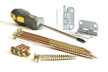 Set of long, medium and short yellow tapping screws, tip of the Phillips screwdriver with rubbery elastic handle and two matt steel door hinges on a white background. Isolated